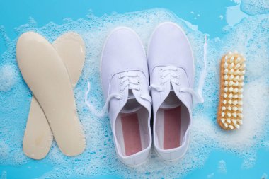 Köpüklü spor ayakkabılar, toz deterjan, su çözeltisi ve mavi arka planda ahşap fırça. Kirli ayakkabıları yıkamak.