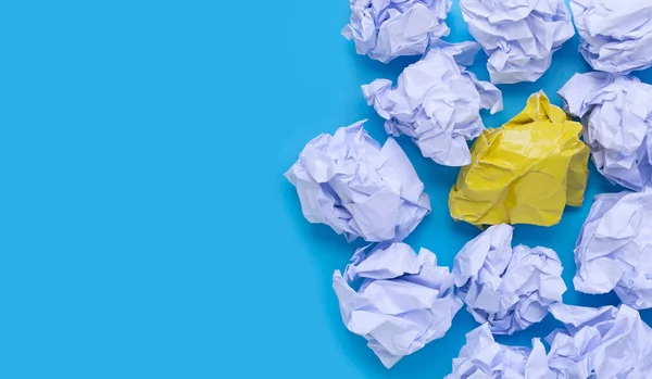 White and yellow crumpled paper balls on a blue background. Top view with copy space