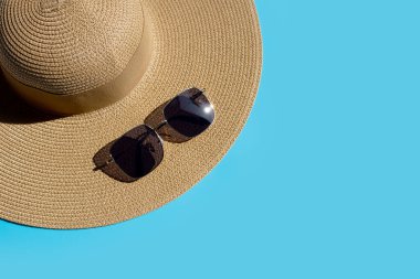 Mavi arka planda güneş gözlüklü yaz şapkası. Tatil kavramının tadını.