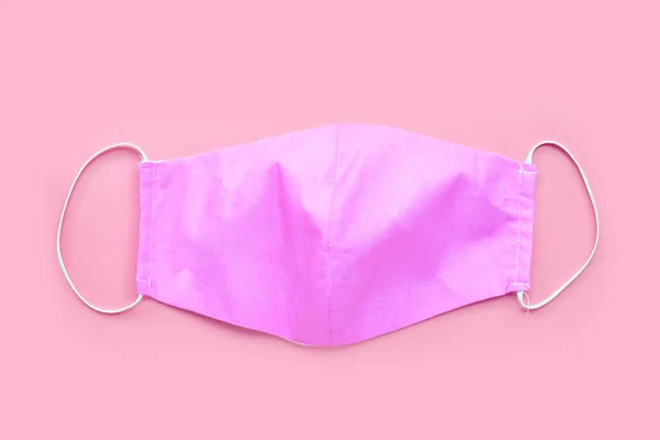 Handmade pink cloth mask on pink background. Top view