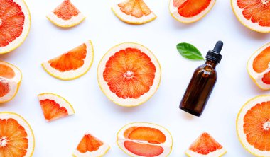 Beyaz arka planda greyfurt dilimleri olan gerekli yağ şişesi. Yüksek C vitamini. 