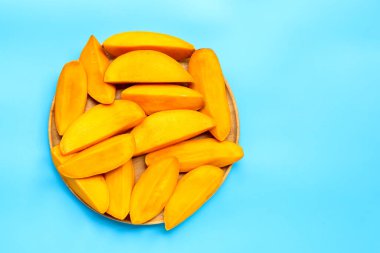 Tropik meyve, mavi arka planda ahşap tabakta mango dilimleri. Üst görünüm