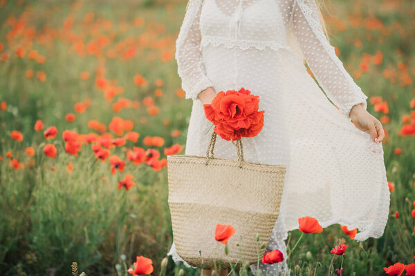 Girl in a white dress with a wicker basket on a poppy field