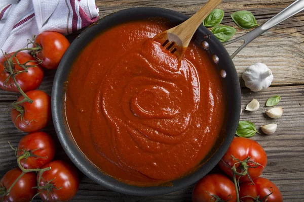 Tavada domates sosu, ahşap spatula ve malzemelerle.