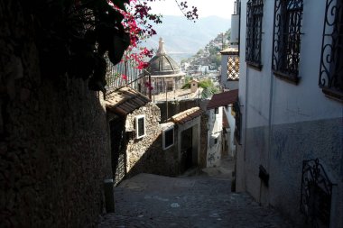 Taxco, Guerrero, Meksika - 2019: Şehrin tipik arnavut kaldırımlı sokaklarından biri, şehir ve dağların uzaklıkmanzarasına sahip. 
