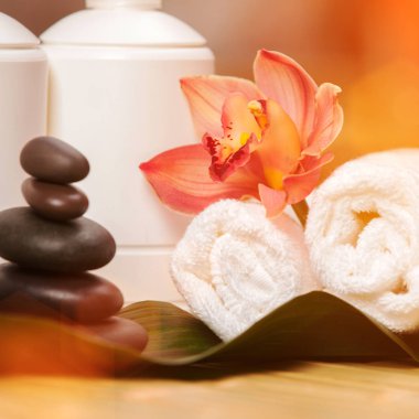 Spa arka planı. Egzotik bitkiler üzerinde beyaz havlular, güzel orkide çiçekleri ve rahatlatıcı spa masajı ve vücut bakımı için dengeleyici taşlar. Aromalı Asya ilaçları ve sağlıklı vücut için taş terapisi.