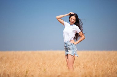 Sahadaki hayattan zevk alan mutlu moda kadını. Doğa güzelliği, mavi gökyüzü ve buğdaylı altın tarla. Açık hava yaşam tarzı. Özgürlük kavramı. Buğday tarlasında bir kadın