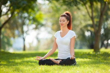 Yoga dışarıda. Yoga egzersizleri yapan, parkta meditasyon yapan mutlu bir kadın. Yoga meditasyonu. Sağlıklı yaşam tarzı ve rahatlama kavramı. Çimenlerde yoga yapan güzel bir kadın.