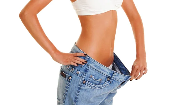 女人穿旧的牛仔裤 孤立的白色背景上显示她减肥 运动和美丽的女性身体的特写 健康的生活方式 重量损失概念 — 图库照片