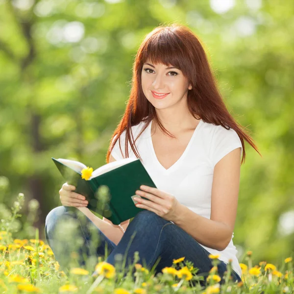 Giovane donna che legge un libro nel parco con dei fiori. Bellezza natu — Foto Stock