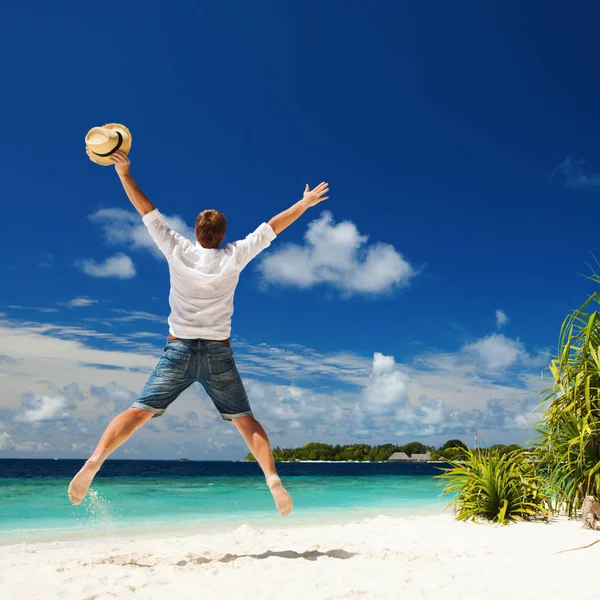 Um homem feliz a saltar na praia tropical. Areia branca, azul nublado — Fotografia de Stock