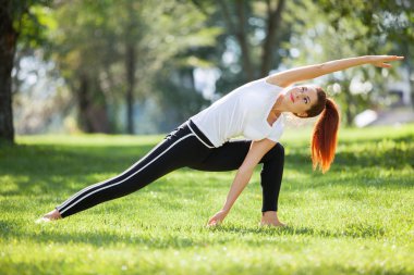 Yoga dışarıda. Yoga egzersizleri yapan, parkta esneme hareketleri yapan mutlu bir kadın. Yoga meditasyonu. Sağlıklı yaşam tarzı ve rahatlama kavramı. Çimenlerde yoga yapan güzel bir kadın.