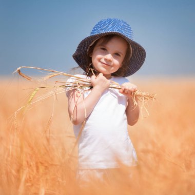 Altın buğdayda yürüyen mutlu kız, tarladaki hayatın tadını çıkarıyor. Doğa güzelliği, mavi gökyüzü ve buğday tarlası. Aile açık hava yaşam tarzı. Özgürlük kavramı. Yaz tarlasında küçük tatlı bir kız.