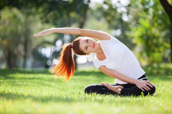 Yoga ao ar livre. Mulher feliz fazendo exercícios de ioga, meditar no parque. Meditação de ioga na natureza. Conceito de estilo de vida saudável e relaxamento. Mulher bonita praticando ioga na grama — Fotografia de Stock