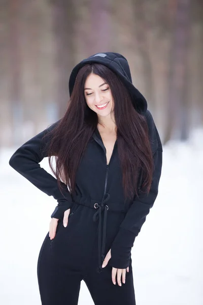 Portrait of beautiful happy stylish woman in overalls, walking at winter forest. Fashion woman lifestyle. Woman style, trendy outfit. Winter vacation. — Stock Photo, Image