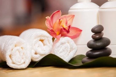 Spa arka planı. Egzotik bitkiler üzerinde beyaz havlular, güzel orkide çiçekleri ve rahatlatıcı spa masajı ve vücut bakımı için dengeleyici taşlar. Aromalı Asya ilaçları ve sağlıklı vücut için taş terapisi.