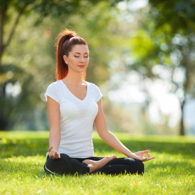 Yoga dışarıda. Yoga egzersizleri yapan, parkta meditasyon yapan mutlu bir kadın. Yoga meditasyonu. Sağlıklı yaşam tarzı ve rahatlama kavramı. Çimenlerde yoga yapan güzel bir kadın.
