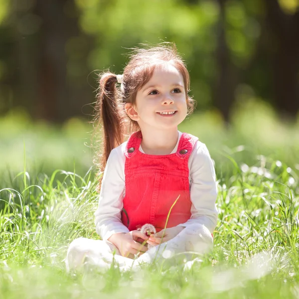 Cute little girl play in the park with flowers. Beauty nature scene with colorful background at summer or spring season. Family outdoor lifestyle. Happy girl relax on green grass — Stock Photo, Image
