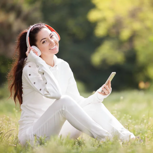 헤드폰을 놓고 공원에서 휴식을 취하는 행복 한 여성. 아름다운 자연 경관에 다채 로운 배경이 있다. 여름에 휴대 전화로 음악을 즐기는 패션 여성. 옥외 생활 방식 — 스톡 사진