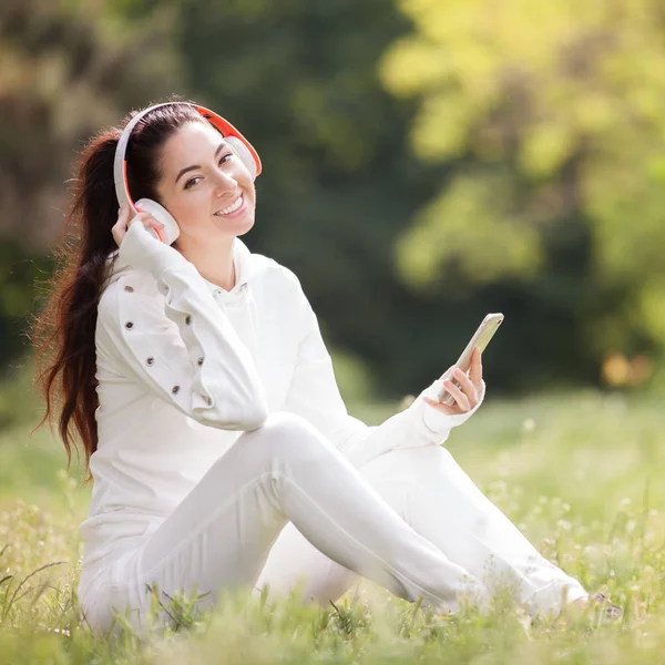 Mujer feliz con auriculares relajándose en el parque. Belleza escena de la naturaleza con fondo colorido. Mujer de moda disfrutando de la música de su teléfono móvil en la temporada de verano. Estilo de vida exterior —  Fotos de Stock