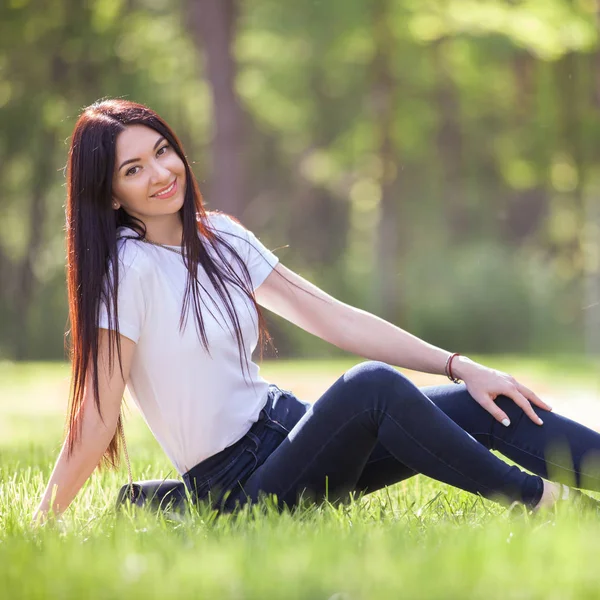 Junge Frau entspannen im Park auf grünem Gras. Schöne Naturszene mit buntem Hintergrund, Bäume zur Sommerzeit. Lebensstil im Freien. Glücklich lächelnde Frau sitzt auf grünem Gras — Stockfoto