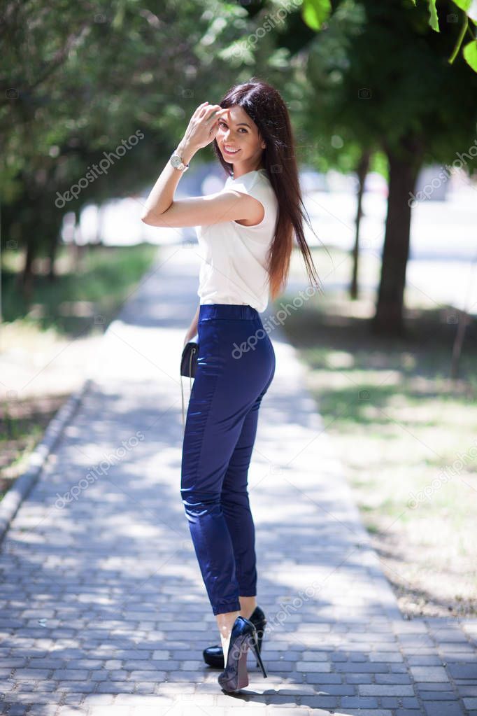 Portrait of beautiful happy stylish woman with long hair in high heels shoes, walking in city park. Woman style, trendy outfit. Fashion lifestyle. Summer woman portrait