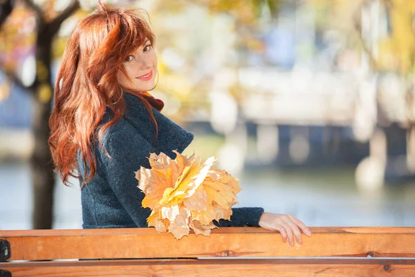 Ung vacker kvinna med rött hår avkopplande i höst park. Skönhet naturen scen med färgglada lövverk bakgrund, gula träd och blad på höstsäsongen. Hösten utomhus livsstil — Stockfoto