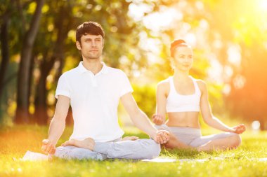 Çiftler Yogası, erkek ve kadın yoga egzersizleri yapıyor, parkta meditasyon yapıyor. Yoga dışarıda. Sağlıklı yaşam tarzı ve rahatlama kavramı. Yoga meditasyonu. Çimenlerde yoga yapan çift.