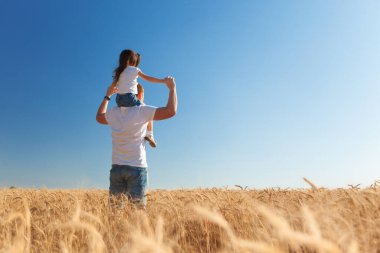 Mutlu baba ve kızı yaz tarlasında yürüyor. Doğa güzelliği, mavi gökyüzü ve altın buğdaylı tarla. Açık hava yaşam tarzı. Özgürlük kavramı.