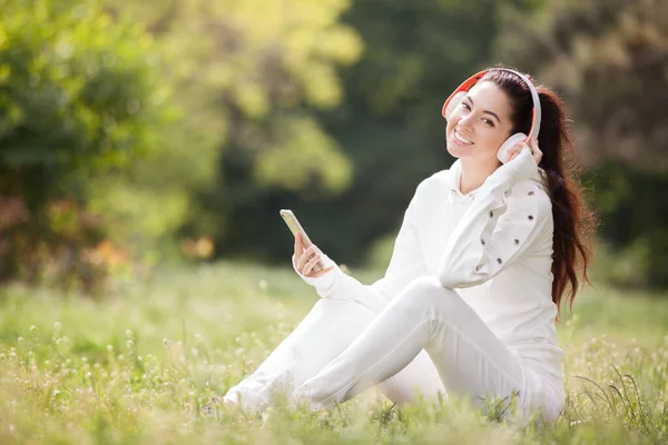 快乐的女人带着耳机在公园里放松 美丽的自然景观 背景五彩斑斓 时尚界的女人喜欢夏天用手机听音乐 户外生活方式 — 图库照片