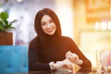 Kahvede kahve içen gülümseyen kadın. Güzel, mutlu, şık bir kadının portresi. Moda yaşam tarzı. Kadın tarzı, modaya uygun kıyafet.