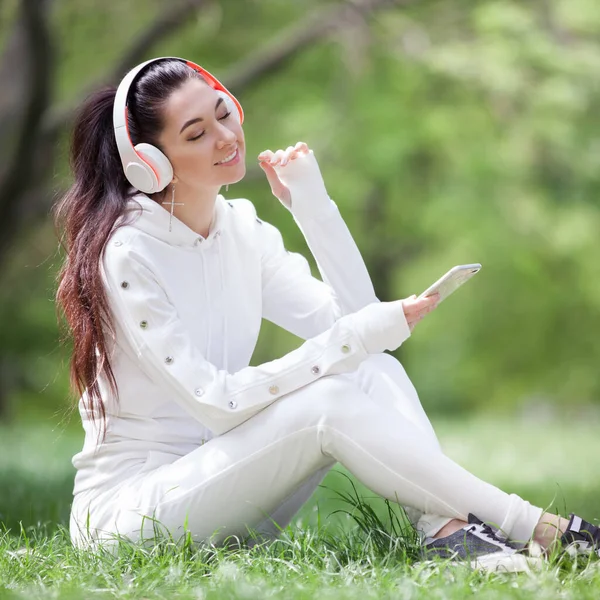 快乐的女人带着耳机在公园里放松 美丽的自然景观 背景五彩斑斓 时尚界的女人喜欢夏天用手机听音乐 户外生活方式 图库图片