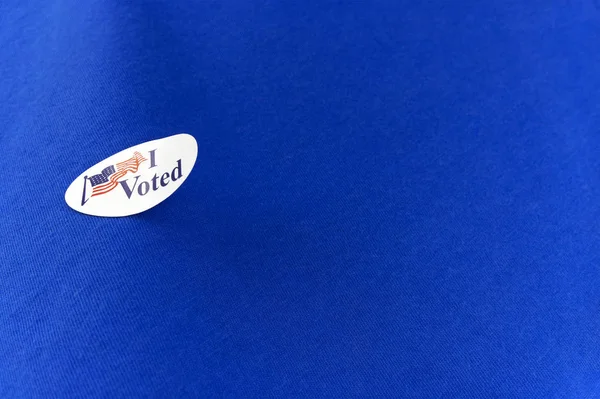 Peeling, curled election voting sticker on a blue cotton clothing shirt.