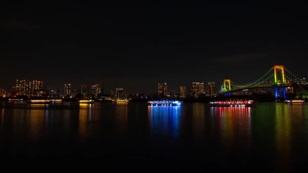 Drijvende schepen in de buurt van de tijdspanne van de regenboog-brug 's nachts — Stockvideo