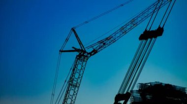 Yapım altında alacakaranlıkta mavi gökyüzünün arkasında hareketli vinçler bir zaman atlamalı