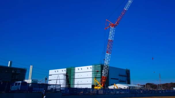 Un lapso de tiempo de grúas en movimiento detrás del cielo azul en el plano ancho en construcción — Vídeo de stock