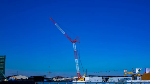 Um lapso de tempo de guindastes em movimento atrás do céu azul no tiro de largura sob construção — Vídeo de Stock