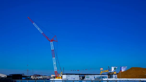 Un lapso de tiempo de grúas en movimiento detrás del cielo azul en el plano ancho en construcción — Vídeo de stock