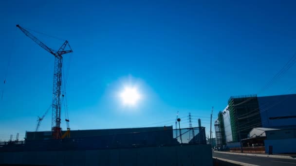 Un lapso de tiempo de grúas en movimiento detrás del cielo azul en el plano ancho en construcción — Vídeo de stock