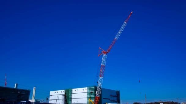 Un lapso de tiempo de grúas en movimiento detrás del cielo azul en el plano ancho en construcción — Vídeos de Stock