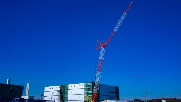 Un lapso de tiempo de grúas en movimiento detrás del cielo azul en el plano ancho en construcción — Vídeo de stock