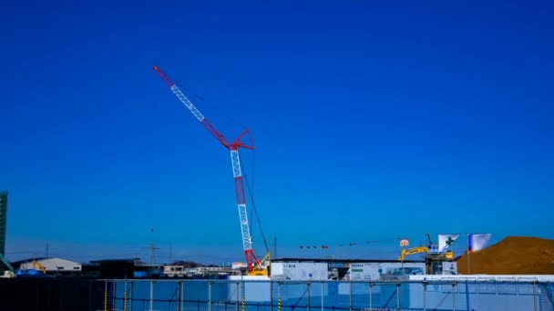 Un time lapse di gru in movimento dietro il cielo blu al colpo largo in costruzione — Video Stock