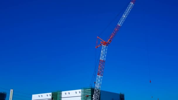 Un lapso de tiempo de grúas en movimiento detrás del cielo azul en el plano ancho en construcción — Vídeos de Stock