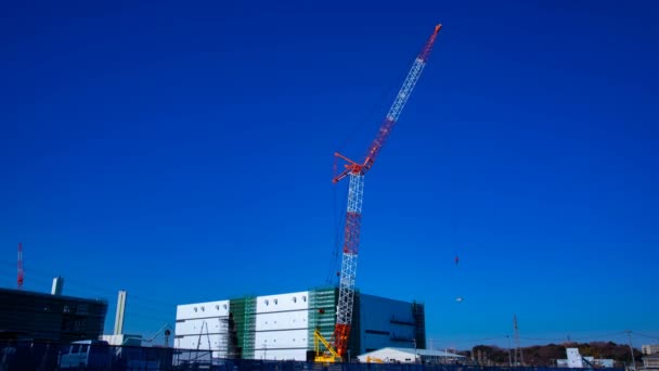 Un lapso de tiempo de grúas en movimiento detrás del cielo azul en el plano ancho en construcción — Vídeo de stock