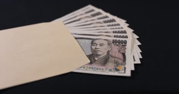 Japońska waluta 100.000 jenów z kopertą na czarnym tle pochylenia — Wideo stockowe