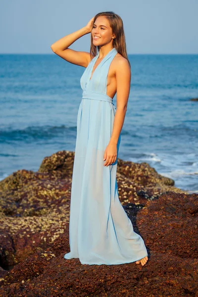 Pełna długość Portret podróżnika Kobieta w niebieskiej sukni szyfonu cieszy się jej tropikalna plaża wakacje stojący na skale fale Oceanu Indyjskiego i niebo tle. atrakcyjny strój dziewczynka lato Odzież kolekcja — Zdjęcie stockowe