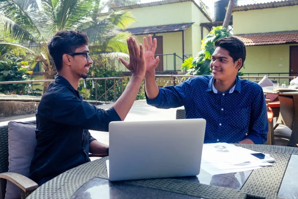 Hindistanlı genç iş adamları, iş adamları, iş adamları, plajda dizüstü bilgisayarla şezlongda çalışıyorlar. İki başarılı arkadaş, tropikal cennette uzak mesafelere sörf yapıyor..