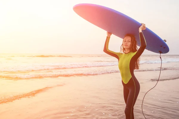 Bella donna in tuta subacquea per il nuoto surf nell'Oceano Indiano sullo sfondo cielo al tramonto e onde.surfista professionista ragazza in muta fare sport in mare.extreme, adrenalina e gioventù — Foto Stock