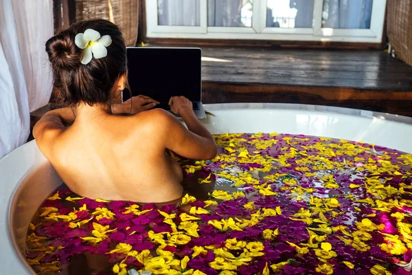 Freelancing y la muchacha work.beautiful remota que trabaja con el ordenador portátil mientras que miente en una bañera con flores tropicales y pétalos, freelance y surfeando en línea.Mujer surfista negocio señora eco hotel Bali vacaciones — Foto de Stock