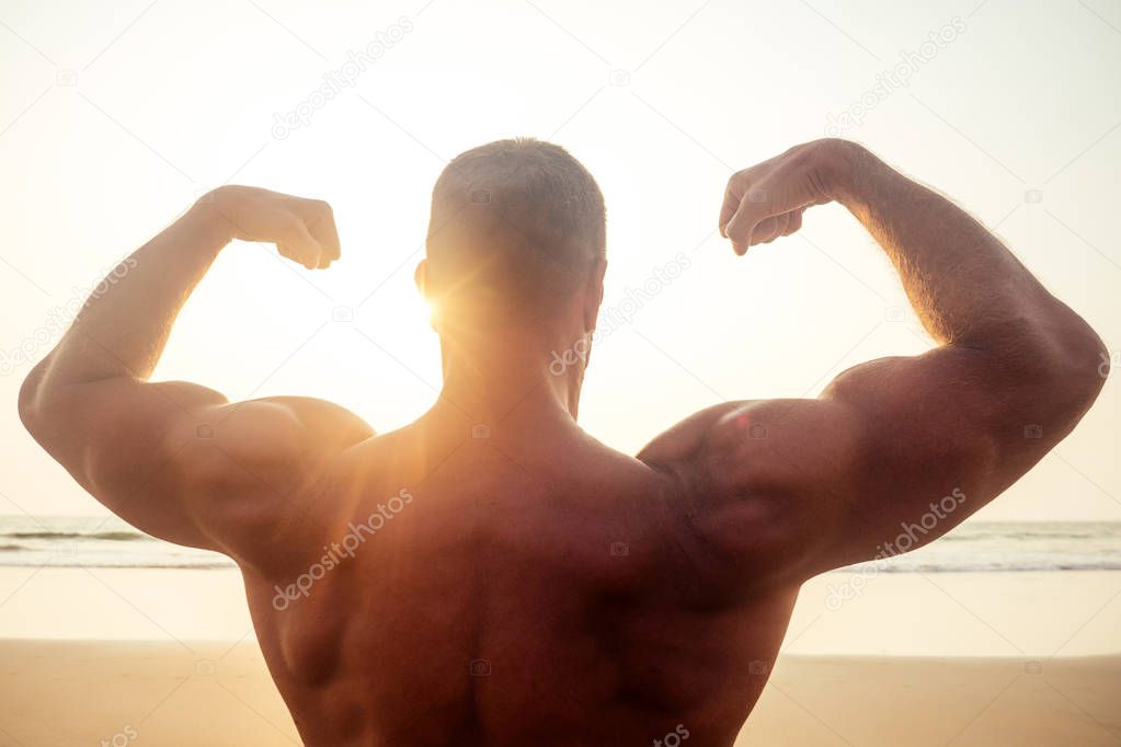 young brutal male bodybuilder shows athletic figure strong torso at sunset on beach .sexy boxers training exercise.